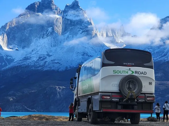 Tour bus parked overlooking a bright blue lake and majestic mountains