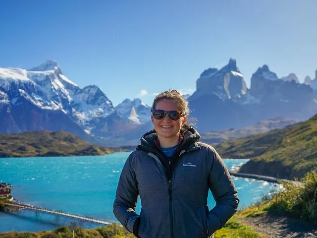 Woman smiling, standing by turquoise lake with snow-capped mountains in Torres del Paine