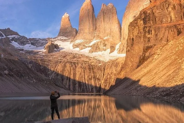 Persona che scatta una foto a tre cime montuose frastagliate che si riflettono in un lago