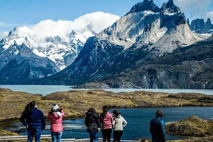 Grupo de personas mirando un lago y enormes montañas nevadas