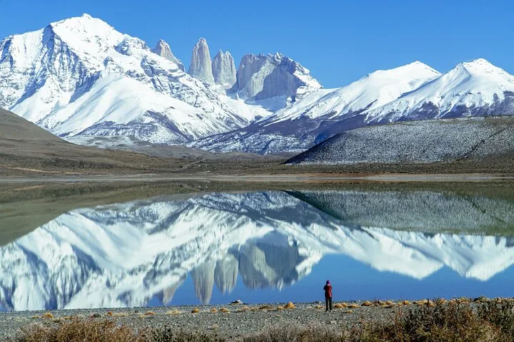 Persona de pie junto a un lago tranquilo que refleja picos nevados en Torres del Paine