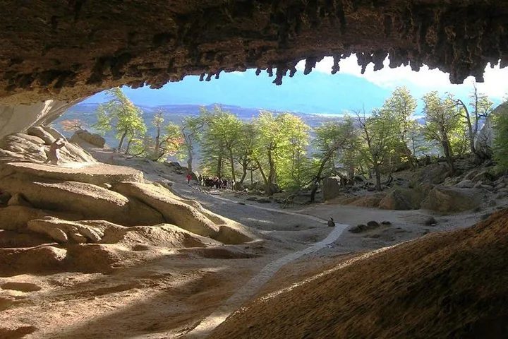 Vista desde el interior de una cueva hacia un sendero, árboles y montañas