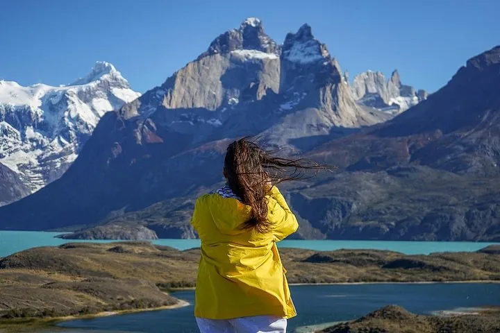 Persona con chaqueta amarilla tomando una foto de una cordillera y un lago